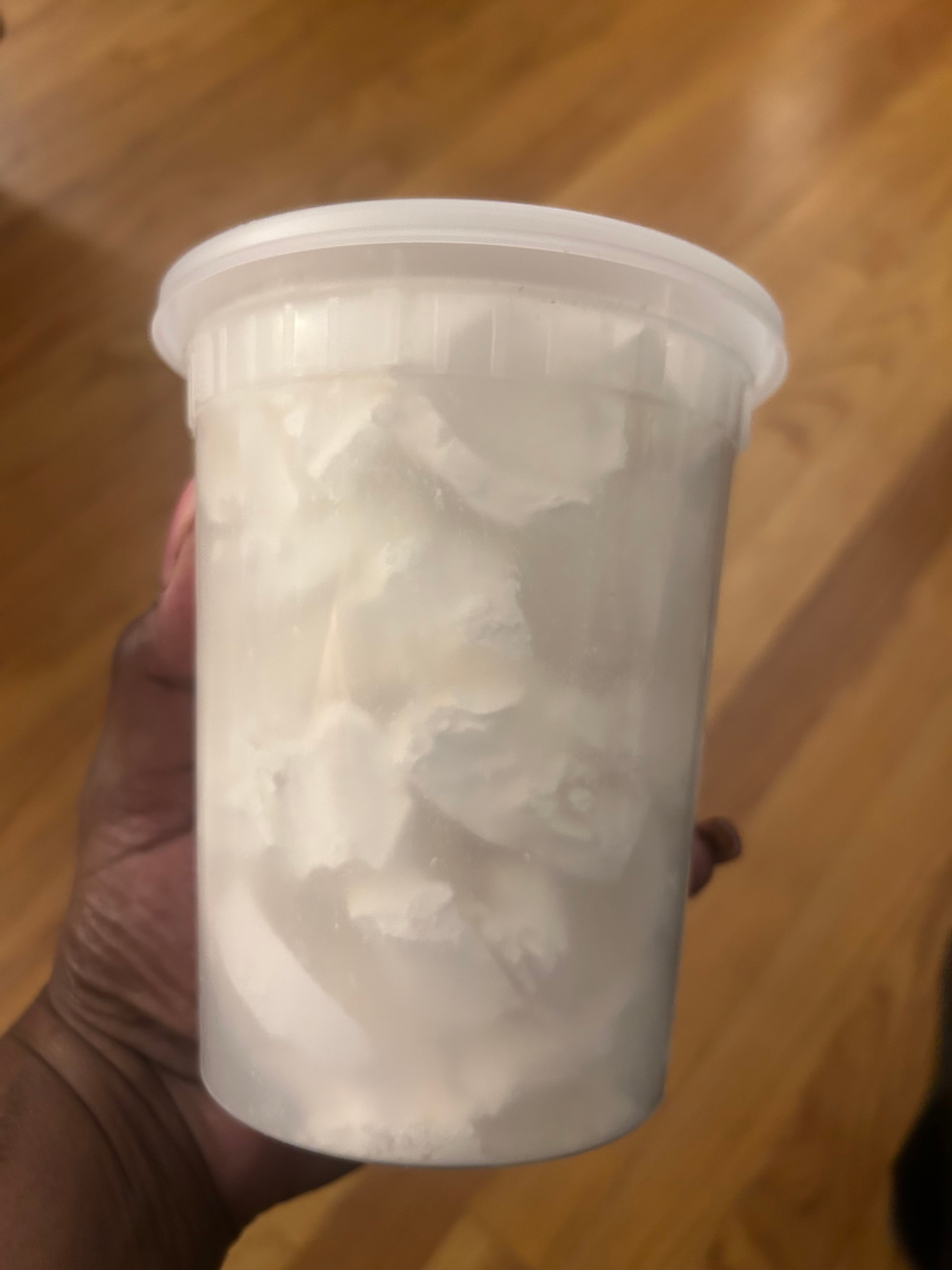 Clear container with white cornstarch held by a hand on a wooden floor.